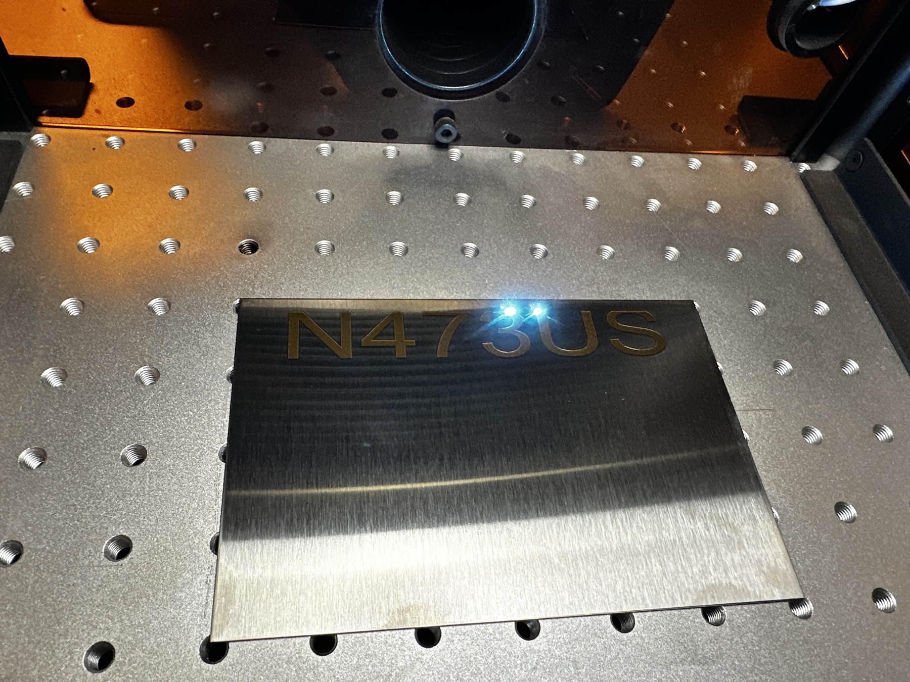 Fiber laser marking an N-number registration plate — N473US being engraved into stainless steel on the AV8 Precision Coatings laser bed